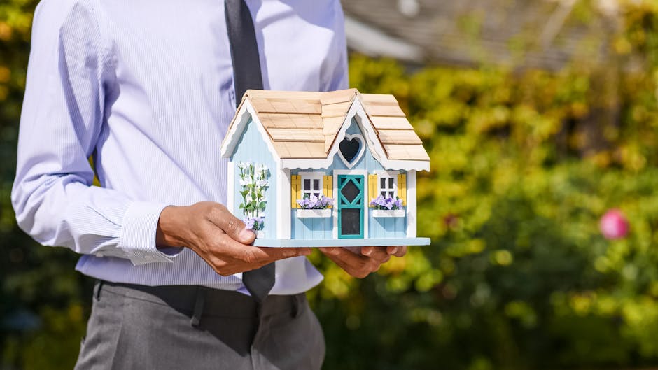 Businessman holds small house model outdoors, symbolizing real estate investment