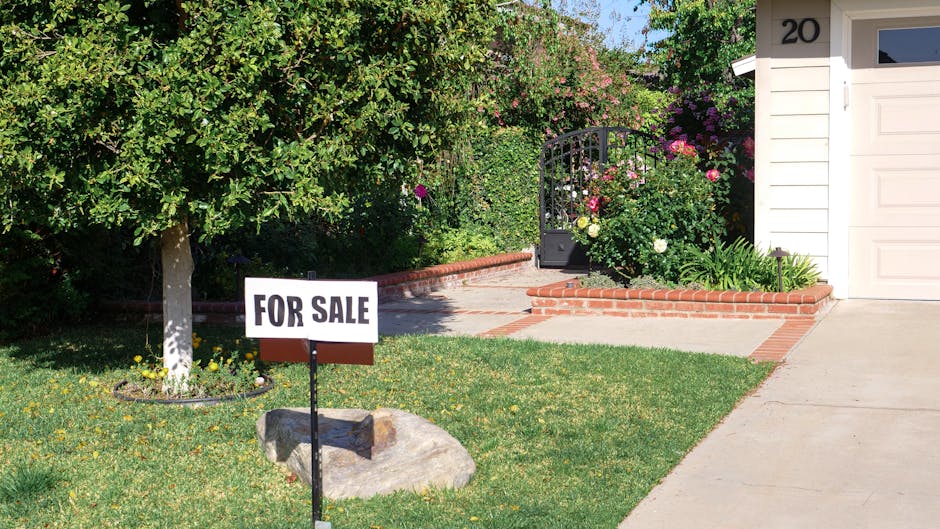 Front view of a house with a garden and 'For Sale' sign in bright daylight